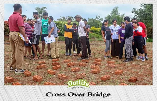 A group of participants strategizing and collaborating to cross a bridge made of bricks during a team-building activity organized by Outlife.