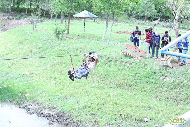  Person enjoying a thrilling zipline ride over a serene grassy area, with a group of people watching in the background